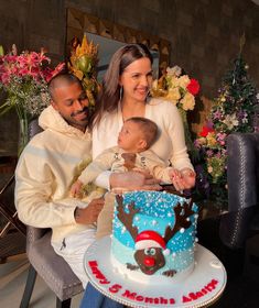 a man and woman holding a baby in front of a christmas cake with reindeer decorations on it