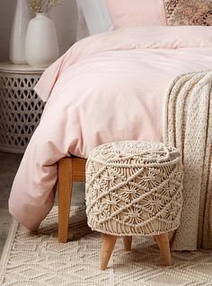 a bed with pink sheets and pillows in a bedroom next to a white vase filled with flowers