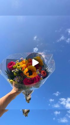 a person holding a bouquet of flowers in their hand with the sky behind them and clouds