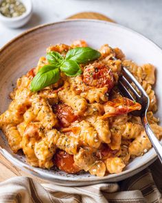 pasta with tomatoes and basil in a white bowl on a wooden table next to a fork