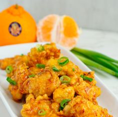 a white plate topped with fried food next to an orange and green onion garnish