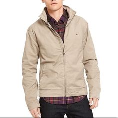 Tan Khaki Jacket With Two Front Pockets, Adjustable Button Cuffs, Two Hidden Pockets On The Inside, Zipper Closure Down The Front And Tommy Emblem On Top Left Casual Tommy Hilfiger Outerwear With Pockets, Casual Outerwear With Button Cuffs For Outdoor, Casual Beige Outerwear With Button Cuffs, Casual Tommy Hilfiger Outerwear For Spring, Tommy Hilfiger Casual Spring Outerwear, Tommy Hilfiger Cotton Long Sleeve Outerwear, Casual Khaki Outerwear With Button Cuffs, Casual Tommy Hilfiger Outerwear With Button Closure, Tommy Hilfiger Casual Outerwear With Button Closure