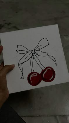 a person holding up a piece of art with two cherries on it