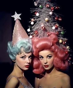 two women with pink and blue hair standing next to each other in front of a christmas tree