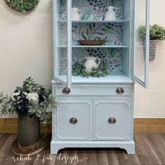 an old china cabinet painted blue and decorated with greenery in the corner, next to a potted plant