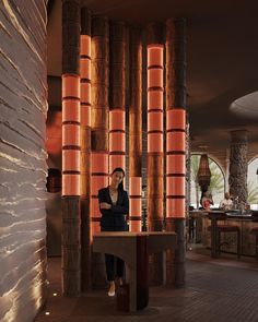 a woman sitting at a table in front of tall bamboo columns with lights on them