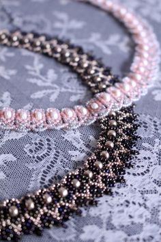 two beaded necklaces sitting on top of a lace covered table cloth next to each other