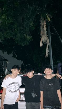 three young men standing next to each other in front of a car at night time