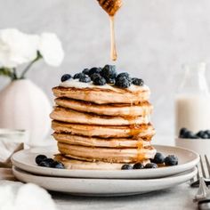 a stack of pancakes with blueberries and syrup being drizzled on top