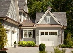 a house with two garages in front of it and bushes around the driveway area