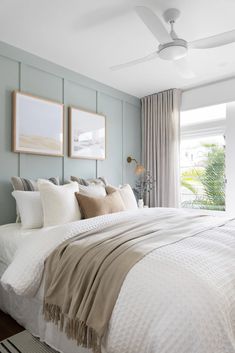 a bedroom with blue walls, white bedding and two framed pictures on the wall