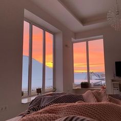 a bedroom with three large windows and a view of the ocean at sunset or dawn