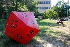 a large red dice sitting on top of a lush green field next to a tall building