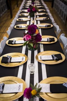 the table is set with black and white striped plates, gold rimmed place settings, and purple flowers