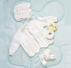 a baby's white outfit and booties laid out on a blue blanket with a teddy bear