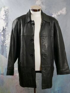 "This 1990s black leather coat has a wing collar and padded shoulders, and closes in the front with four black buttons. The coat has two hip pockets on the front, and is fully lined in a black satin rayon fabric (with two inner zippered pockets). Note that this is a \"short\" size (46S). Brand label: Dönmez Size: 46S US/UK Material: Genuine Leather Chest = 48 inches (121.92cm)(This is a Size 46S US/UK; the extra 2 inches here allow for what you wear under.) Shoulder Width = 21 inches (53.34cm) S Classic Black Leather Jacket With Button Closure, Winter Leather Outerwear With Snap Closure, Classic Black Leather Jacket With Double Button Closure, Classic Black Leather Long Coat, Classic Black Long Leather Jacket, Black Vintage Outerwear With Double Button Closure, Vintage Black Leather Jacket With Button Closure, Black Vintage Leather Jacket With Button Closure, Steampunk Jacket