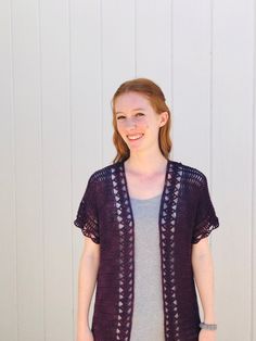 a woman standing in front of a white wall wearing a purple cardigan and jeans