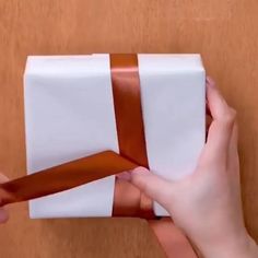 someone is wrapping a gift in white paper with brown ribbon on the top and bottom