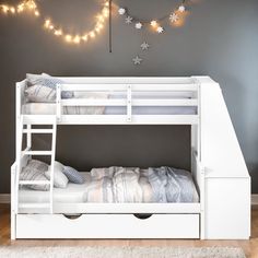 a white bunk bed sitting next to a wall with string lights on top of it