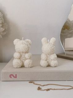 two small white teddy bears sitting on top of a book next to a flower vase