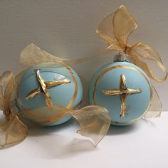 two blue christmas balls with gold trim and a cross on the top, one has a ribbon tied around it