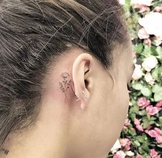 a woman's left ear has a small flower tattoo on the back of her right ear