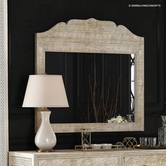 a large mirror sitting on top of a white dresser next to a lamp and vase