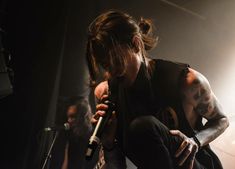 a woman sitting on top of a stage with a microphone in her hand and another person standing behind her