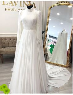 a white wedding dress with long sleeves and a high neckline is displayed in front of a mirror