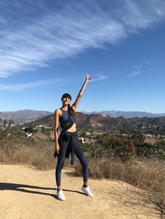 a woman standing on top of a dirt road with her arms up in the air