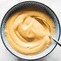 a spoon is in a bowl filled with peanut butter and mustard sauce on a white tablecloth