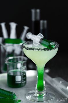 a green and white drink in a glass with some bottles behind it on a tray