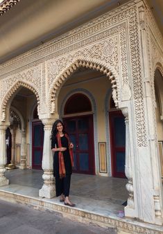 a woman standing in front of a building with columns and arches on the side walk