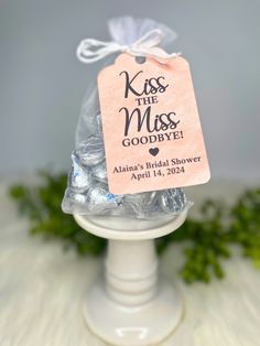 a bag of hers kisses on top of a white cake stand with a tag that says kiss the miss goodbye