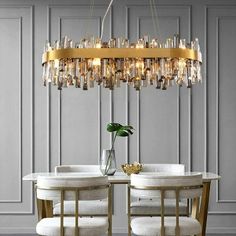 a modern chandelier hanging over a dining room table with chairs and a vase