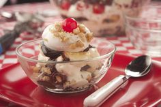 an ice cream sundae with cherries in a glass bowl on a red tray