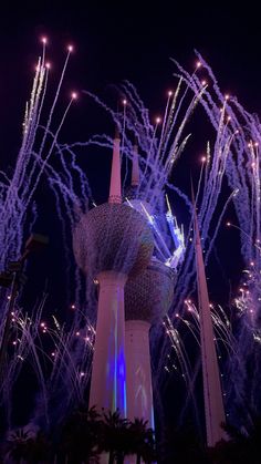 fireworks are lit up in the night sky behind a tall building with a clock on it