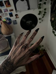 a person's hand with black nail polish and skeleton print on it, in front of a white wall