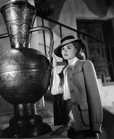 a woman standing next to a large vase and looking at the camera while wearing a hat