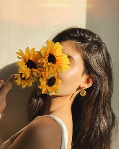 a woman with sunflowers in her hair is looking at the camera while she's holding it up to her face