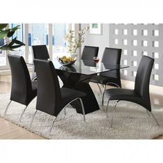 a glass dining table with black chairs and a bowl of fruit on the rug in front of it