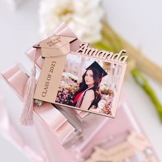 a graduation card with a pink ribbon attached to it and a flower in the background