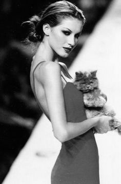 a woman is holding a cat in her hands and posing for the camera while wearing a dress