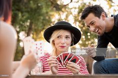 a man and woman playing cards in the back yard with one holding up his hat