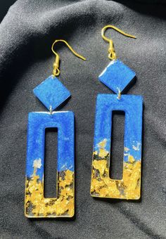 two blue and yellow earrings sitting on top of a black cloth