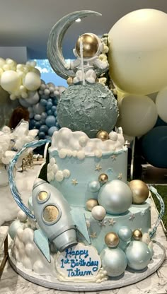 a blue and white cake with balloons in the background