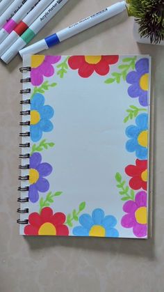 an open notebook with colorful flowers on it next to markers and a potted plant