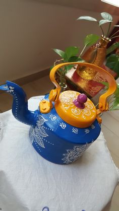 a blue tea pot sitting on top of a white table cloth next to a plant