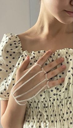 a woman in a white dress with pearls on her hand and an open pearl bracelet