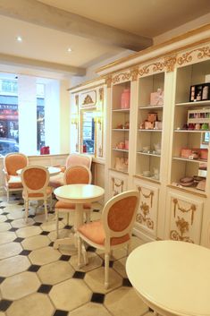 the inside of a restaurant with tables, chairs and shelves filled with cakes on display